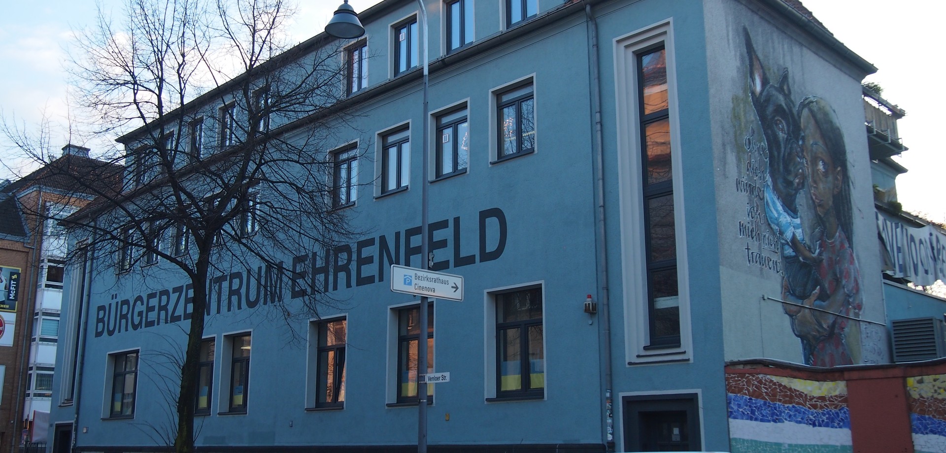 Ein Gebäude auf dem in großen Buchstaben Bürgerzentrum Ehrenfeld steht. Auf der Seitenwand ist ein großes Graffiti von einem Mädchen und ihrem Hund zu sehen.