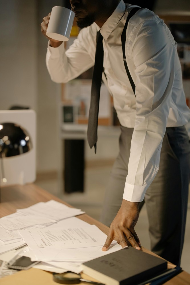 Papierblätter auf dem Tisch, Mann mit weißem Hemd und Krawatte steht gebückt darüber.