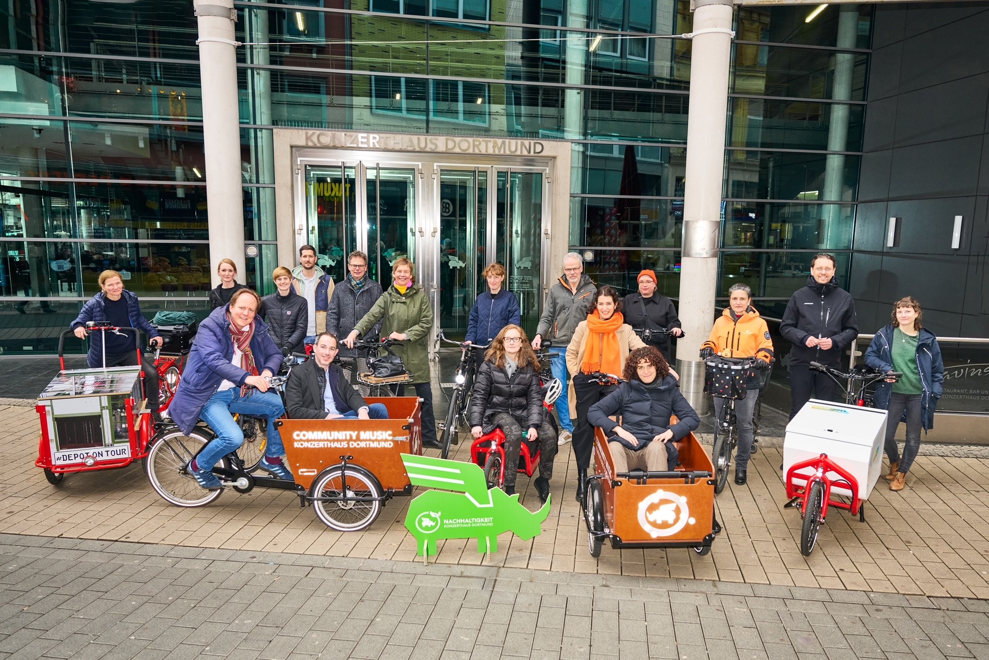 Verschiedene Menschen stehen mit Fahrrädern und Lastenrädern in einer Reihe.