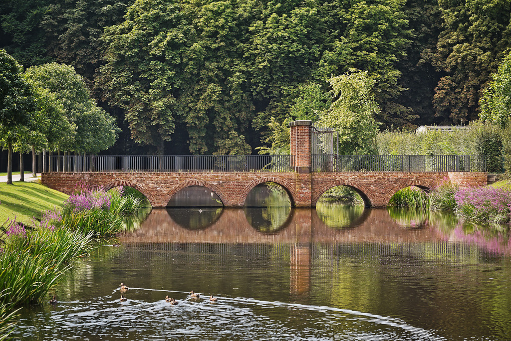 Eine gemauerte Brücke führt über einen Teich