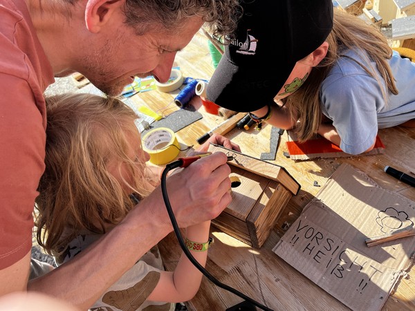 Erwachsener und Kinder arbeiten an einem Holzhäuschen bei einem Upcycling-Workshop.