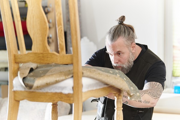 Raumausstattermeister und Polsterer Dennis Mönnekemeyer bei der Arbeit an einem Stuhl.