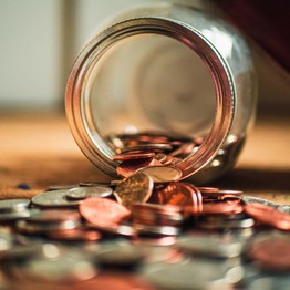 Ein Glas liegt umgekippt auf einem Tisch. Geldmünzen haben sich aus dem Glas auf den Tisch ergossen.