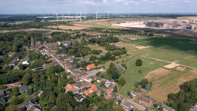 Rheinisches Revier mit kleiner Ortschaft am Waldrand, Braunkohletagebau und Windrädern