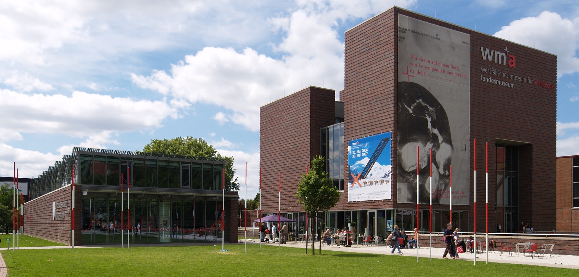Das LWL-Museum für Archäologie. Ein modernes Gebäude. Davor befindet sich eine Wiese und ein Weg über den Menschen gehen.