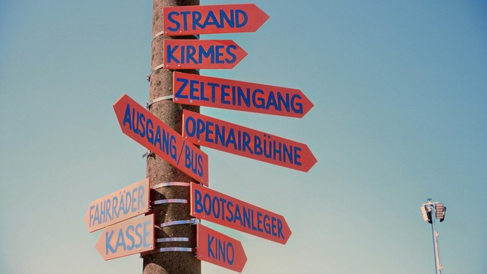 Laternenpfahl vor blauem Himmel mit roten Wegweisern