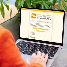 Eine Person sitzt am Laptop. Auf dem Bildschirm ist die Website der Materialbörse Münsterland abgebildet.