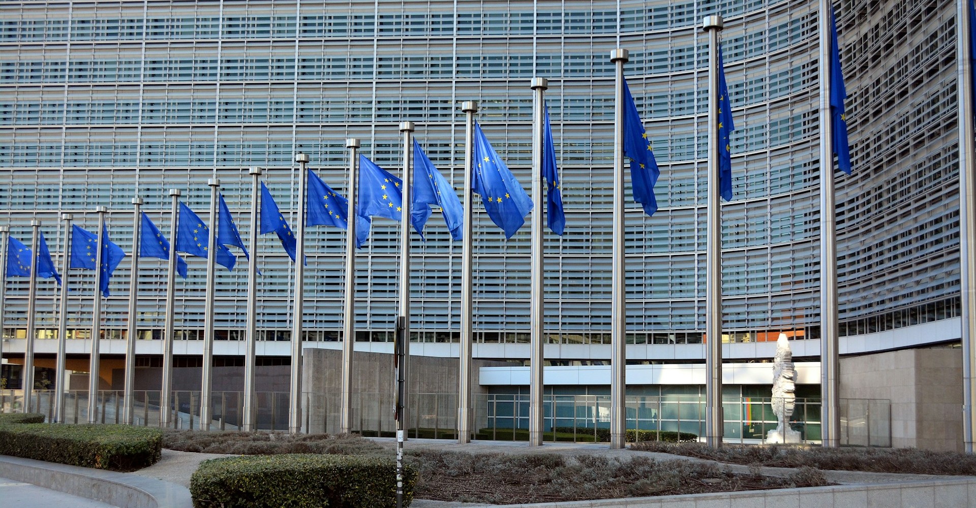 Vor einem hohen gläsernen Gebäude hängen viele EU-Flaggen in einer Reihe.