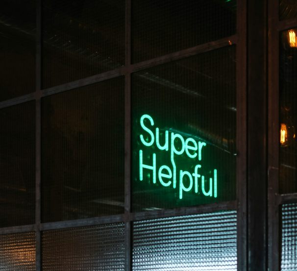 Ein Neon-Schriftzug "Super Helpful" in türkis  ist an einer Glastürfront angebracht.