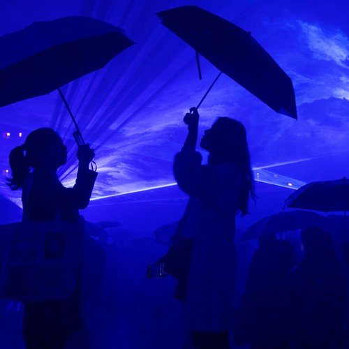 Die Umrisse zweier Personen, die je einen Regenschirm halten. Alles ist in dunkles, bläuliches Licht getaucht.