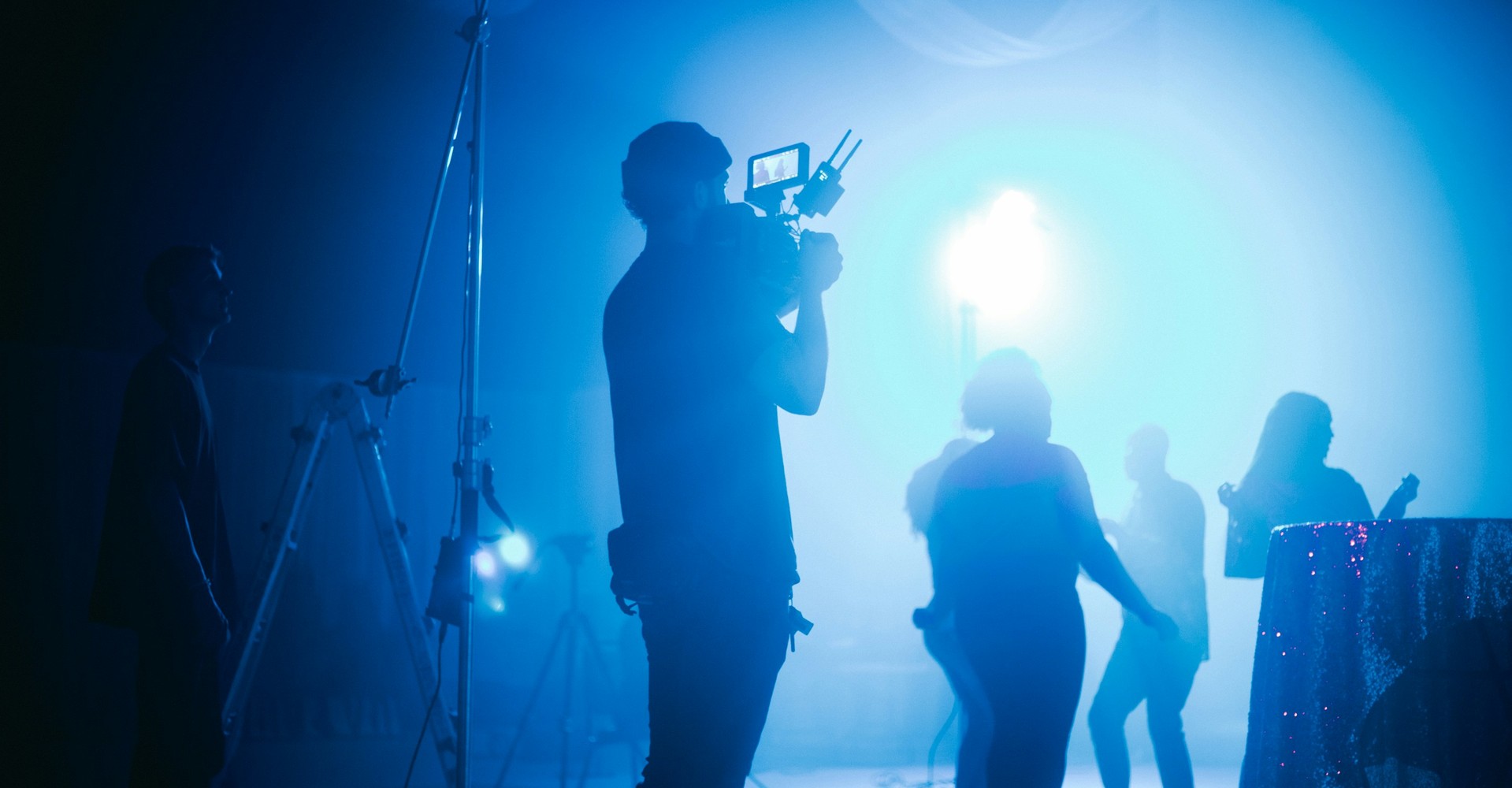 Ein Mann im Vordergrund filmt vier tanzende Menschen vor blauem Licht