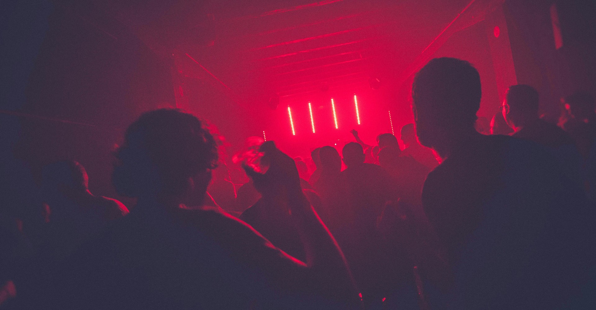 Tanzende Menschen im Club, Scheinwerfer tauchen den gesamten Raum in rotes Licht.