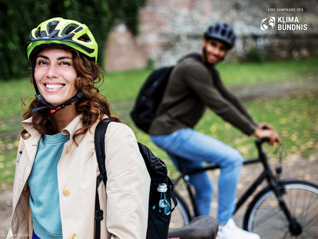 Eine Frau mit Fahrradhelm, im Hintergrund ein Mann auf dem Fahrrad mit Fahrradhelm