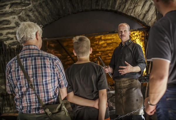 Ein Handwerker stellt Zuschauer:innen seine Arbeit in einer Schmiede vor