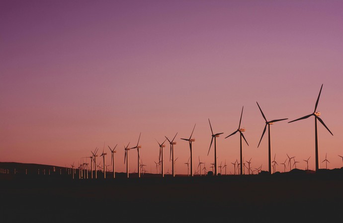 eine Reihe Windräder vor rosafarbenem Himmel