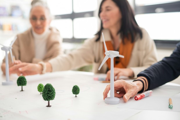 Menschen sitzen an einem Modell mit Windkraftanlagen