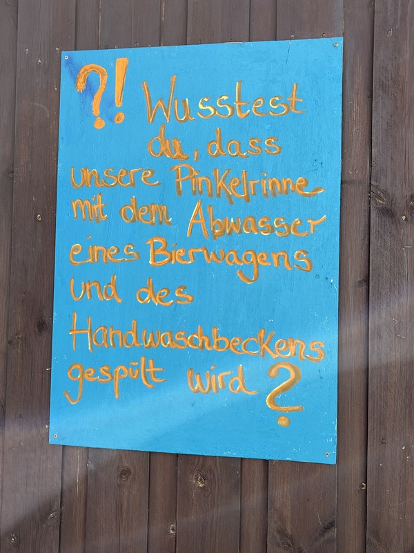 Blaues Hinweisschild mit handgeschriebener Frage zur Nutzung von Abwasser an einer Holzwand.