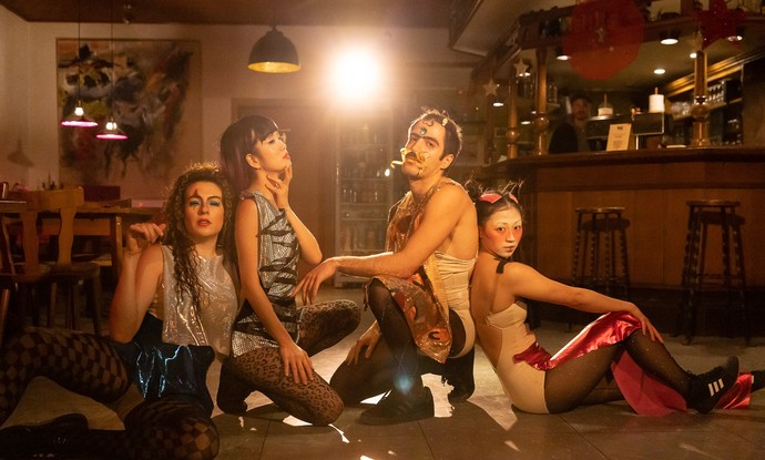 Vier Personen auf dem Boden im Scheinwerferlicht.