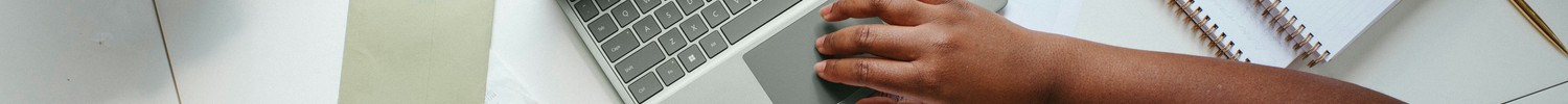 Eine Frau sitzt am Schreibtisch, auf dem Büroutensilien, ein Laptop, ein Taschenrechner, eine Tasse Kaffee und eine Topfpflanze aus Vogelperspektive