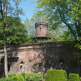 Eine alte Backsteinmauer im Grünen. Dahinter ragt ein Turm aus Backstein hervor.