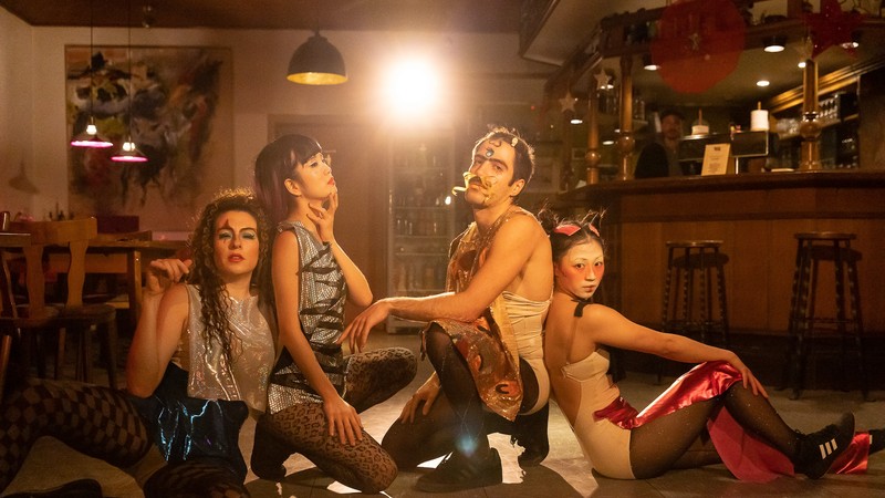 Vier Personen auf dem Boden im Scheinwerferlicht.