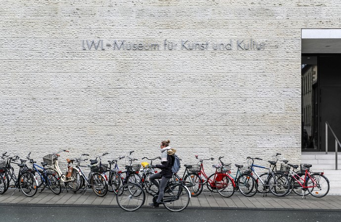 Fahrräder und Fahrradfahrerin vor der Außenfassade des LWL-Museums für Kunst und Kultur