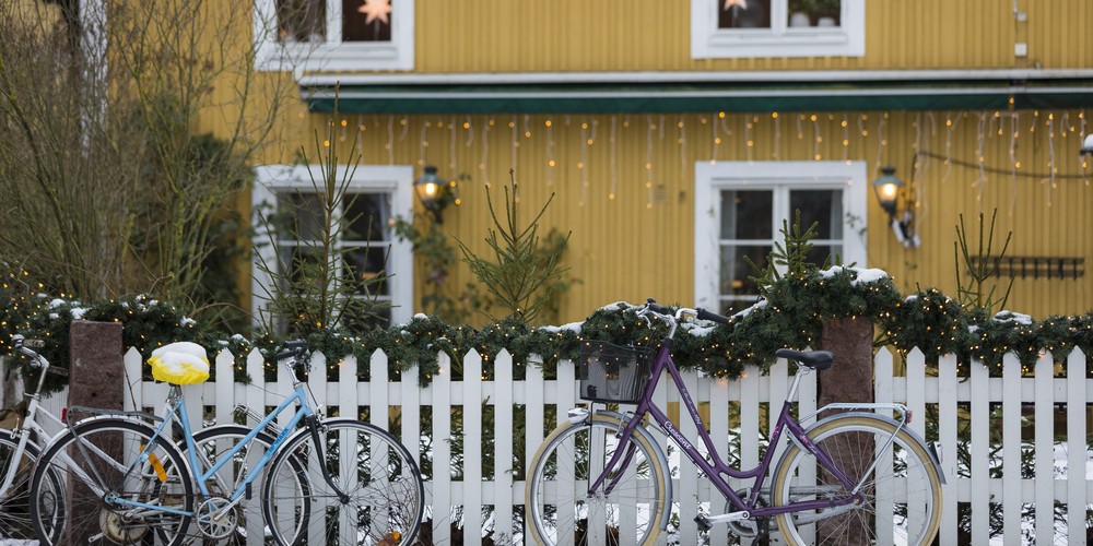 Zwei Fahrräder stehen vor einem weißen Zaun, der ein gelbes Haus im Hintergrund umzäunt.