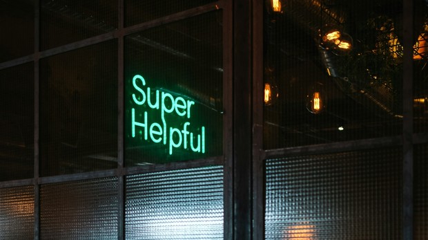 Ein Neon-Schriftzug "Super Helpful" in türkis  ist an einer Glastürfront angebracht.