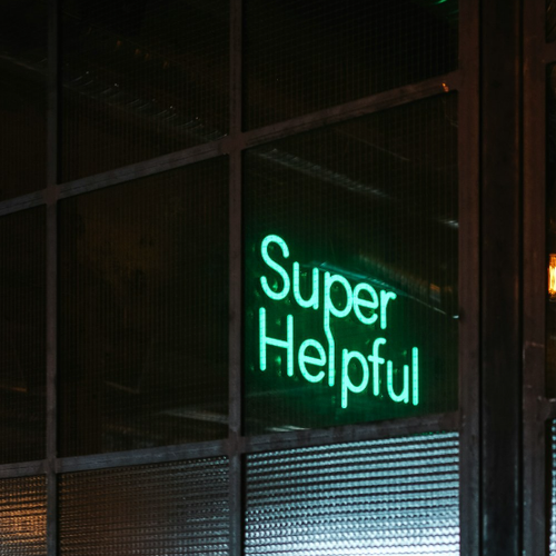 Ein Neon-Schriftzug "Super Helpful" in türkis  ist an einer Glastürfront angebracht.