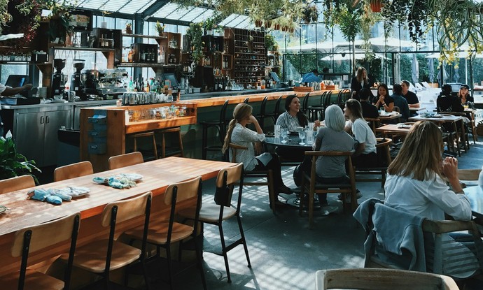 Menschen sitzen in einem Café, welches in einem Glashaus ist.