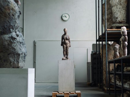 Blick auf eine Steinfigur in einem Lagerraum mit Regalen, auf denen weitere Skulpturen und Gemälde gelagert werden.