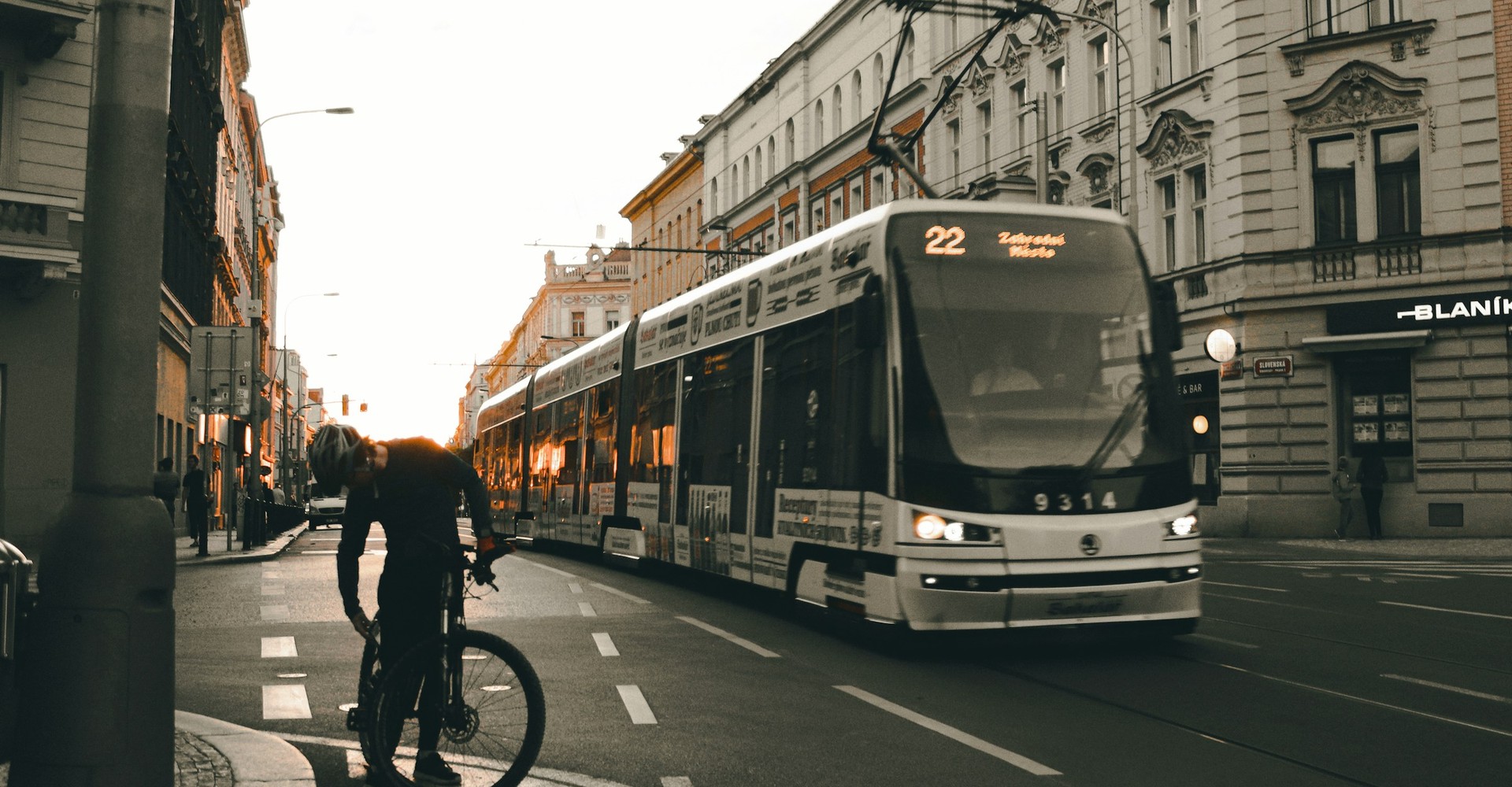 Eine Straßenbahn fährt durch eine Straße im Sonnenuntergang, daneben steht ein Fahrradfahrer.