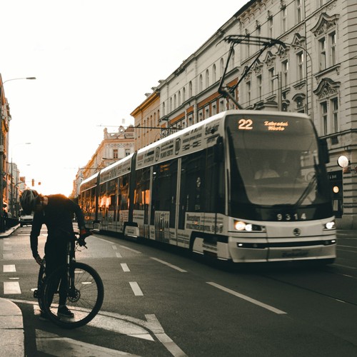 Eine Straßenbahn fährt durch eine Häuserzeile. Links steht ein Fahrradfahrer.